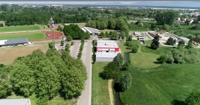 Ansicht auf eine Wiese mit Firmengebäude; links davon ein Sportplatz