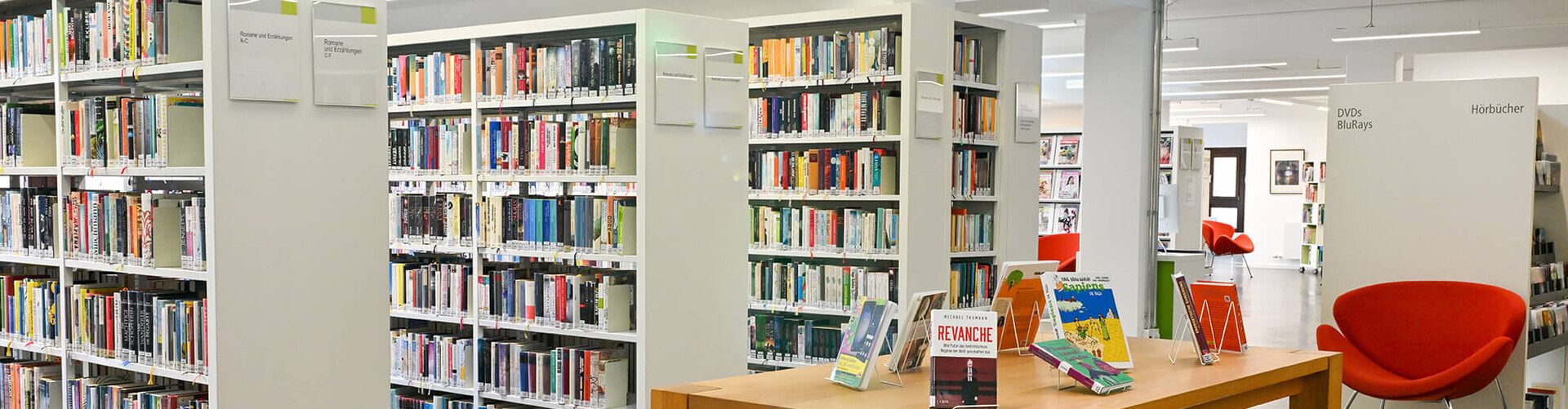 Räumlichkeiten der Bücherei mit Regalen, Ausstelltischen und einem Sessel Header_Medien.jpg