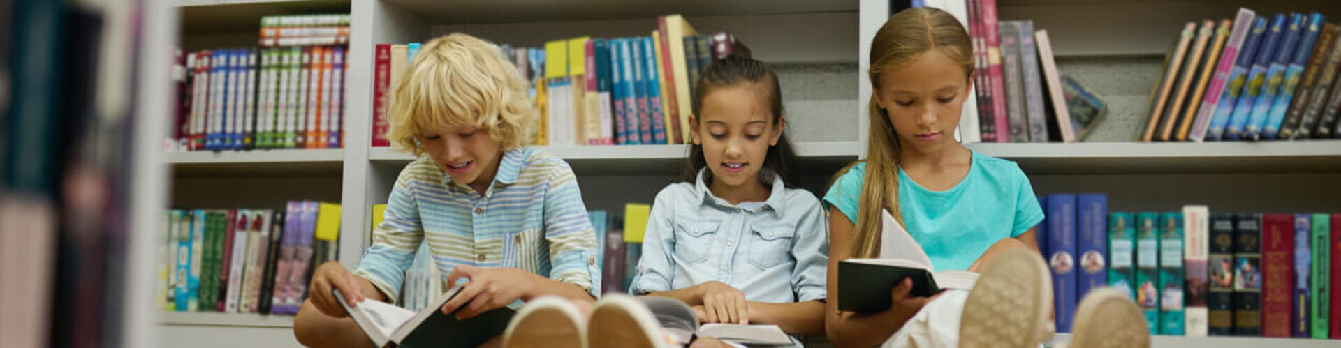 3 Kinder sitzen gemeinsam vor einem Bücherregal auf dem Boden und lesen Header_Kita_und_Schule.jpg
