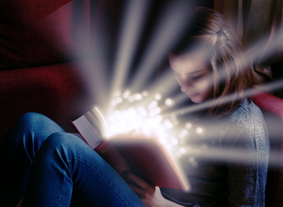 Mädchen sitzt und hat geöffnetes Buch auf dem Schoß aus dem es leuchtet