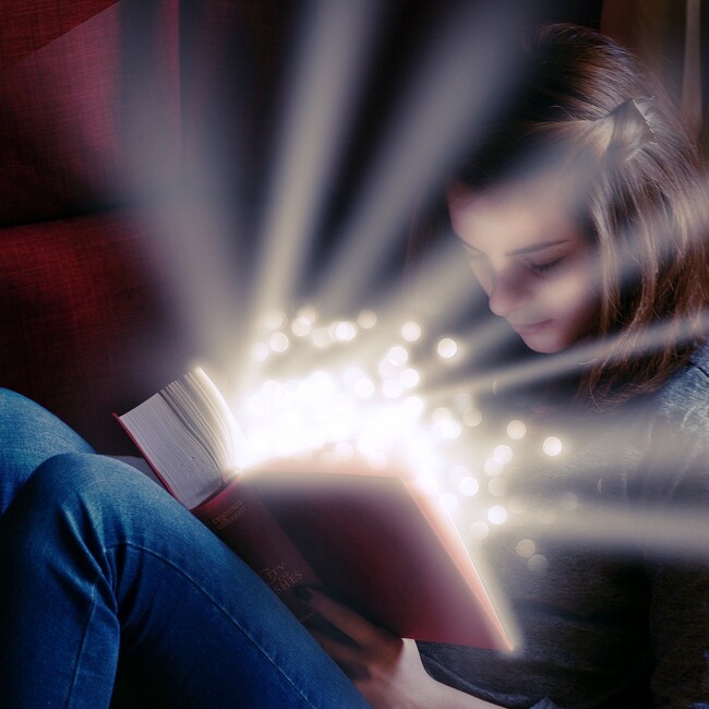 Mädchen sitzt und hat geöffnetes Buch auf dem Schoß aus dem es leuchtet