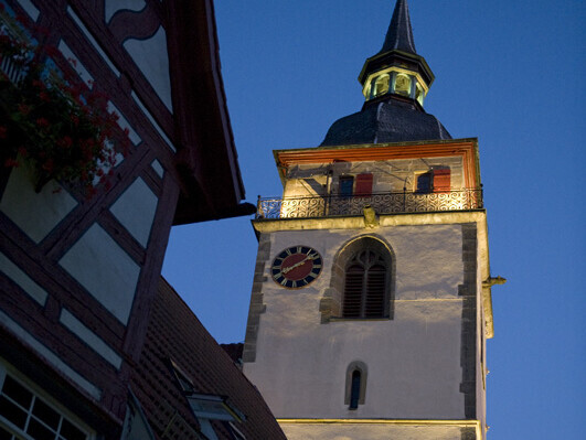 Beleuchteter Kirchturm neben einem Fachwerkhaus