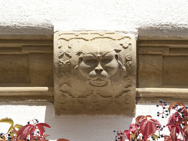 Hauswandverzierungen aus Sandstein. Löwenkopf mit Meanderband