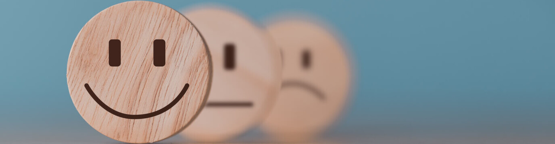 Bild von drei Holzmünzen mit lachenden, neutralen und traurigen Emojis Header_Feedback.jpg
