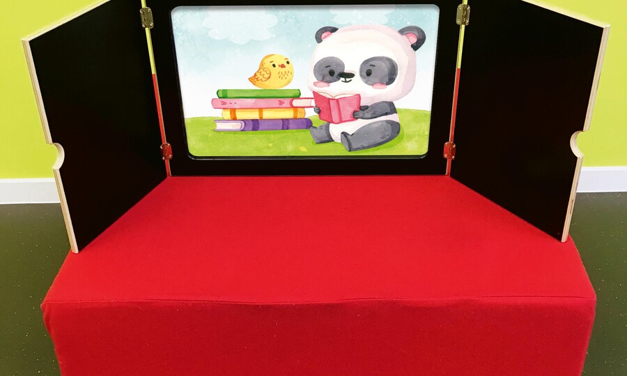ein aufgeklapptes Kamishibai auf rotem Sockel mit einem Bild auf dem ein lesender Panda zu sehen ist