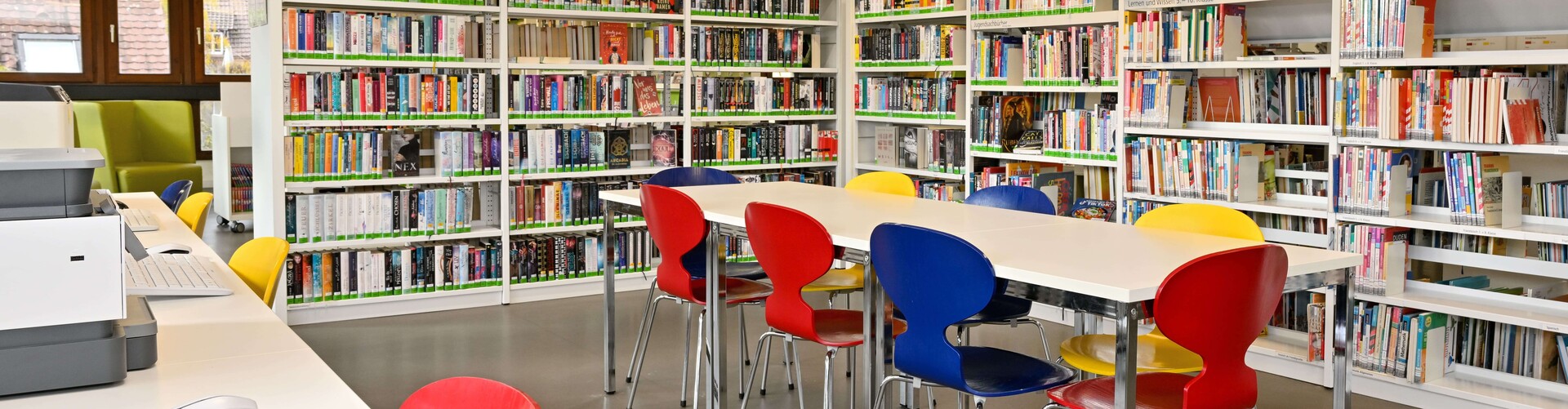 Lernbereich der Jugendbücherei: Zu sehen sind Tische mit Stühlen, Computerarbeitsplätze und Bücherregale Header_weiterfuehrende_Schule.jpg