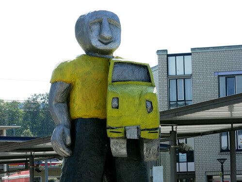 Skulptur "Taxidriver" mit Häusern im Hintergrund