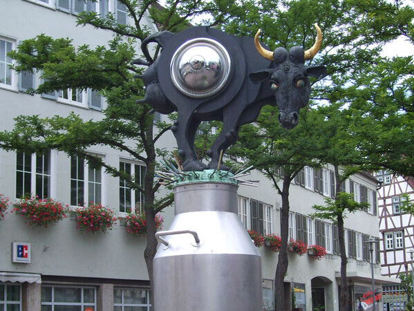 Ansicht auf das Kuhriosum mit Brunnen, an dem eine Frau mit Kind sitzen und Eis essen