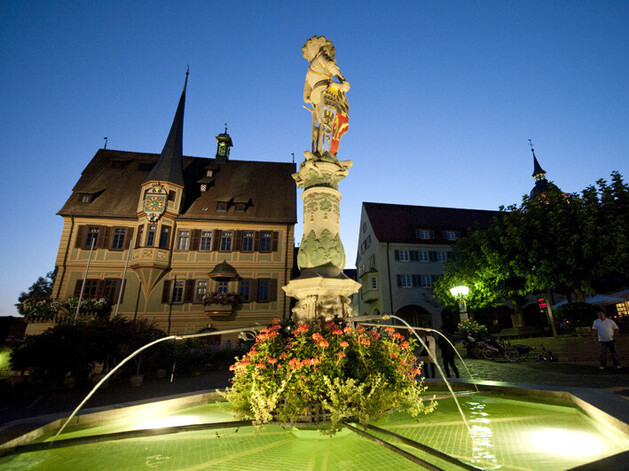 Fachwerkhaus mit Turm und im Vordergrund ein beleuchteter brunnen
