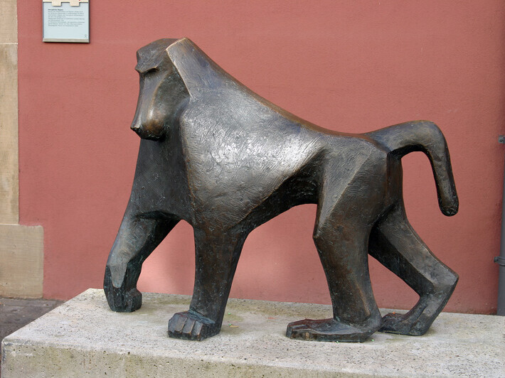 Skulptur eines Pavians auf Stein mit roter Wand im Hintergrund