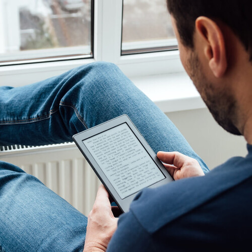 Sitzender Mann mit hochgelegten Beinen liest auf einem E-Reader ein e-Book Header_Digitale_Medien.jpg